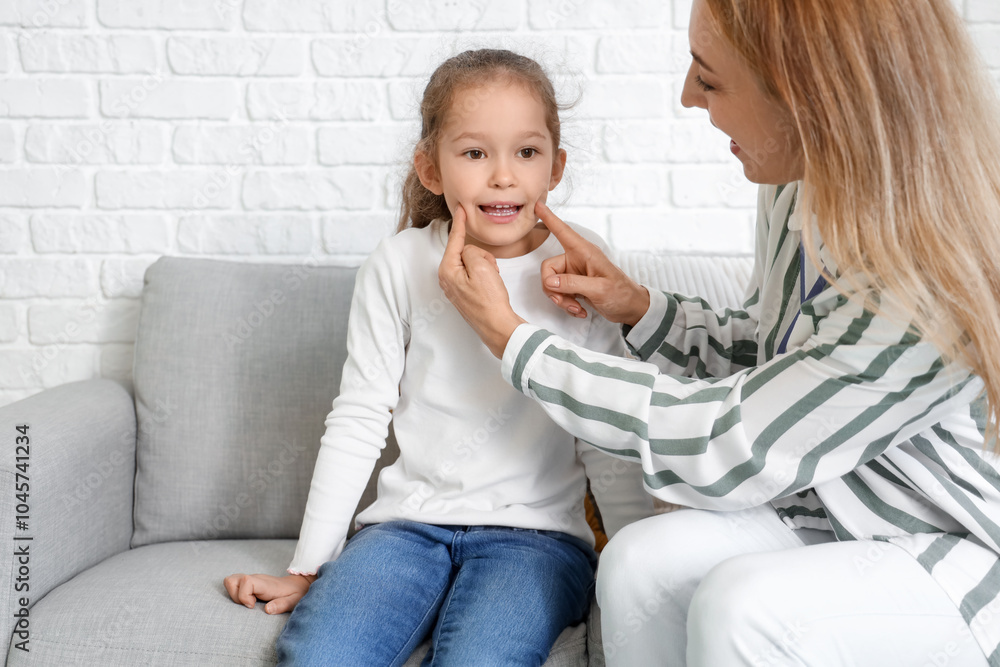 Mature speech therapist working with little girl on sofa in office