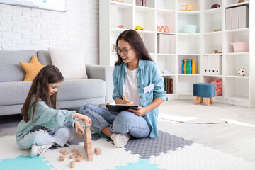 Canvas Print - Female Asian speech therapist writing on clipboard and little girl in office