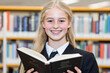 © Konstiantyn Zapylaie - Smiling student in library holding book with shelves in background