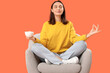 © Pixel-Shot - Young woman with cup of tea meditating in armchair on orange background