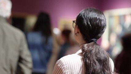 Wall Mural - Back view of pretty Caucasian woman wear eyeglasses and listen to guide. Excursion to museum or an art gallery. Museum day and cultural education