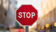 © hardvicore - Stop road sign. Red octagon with white lettering. Blurred city bokeh on background.