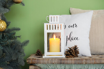 Pillows, cones and Christmas lantern with burning candle near green wall at home