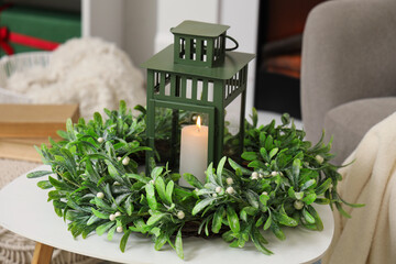 Christmas lantern with burning candle and wreath on table at home, closeup