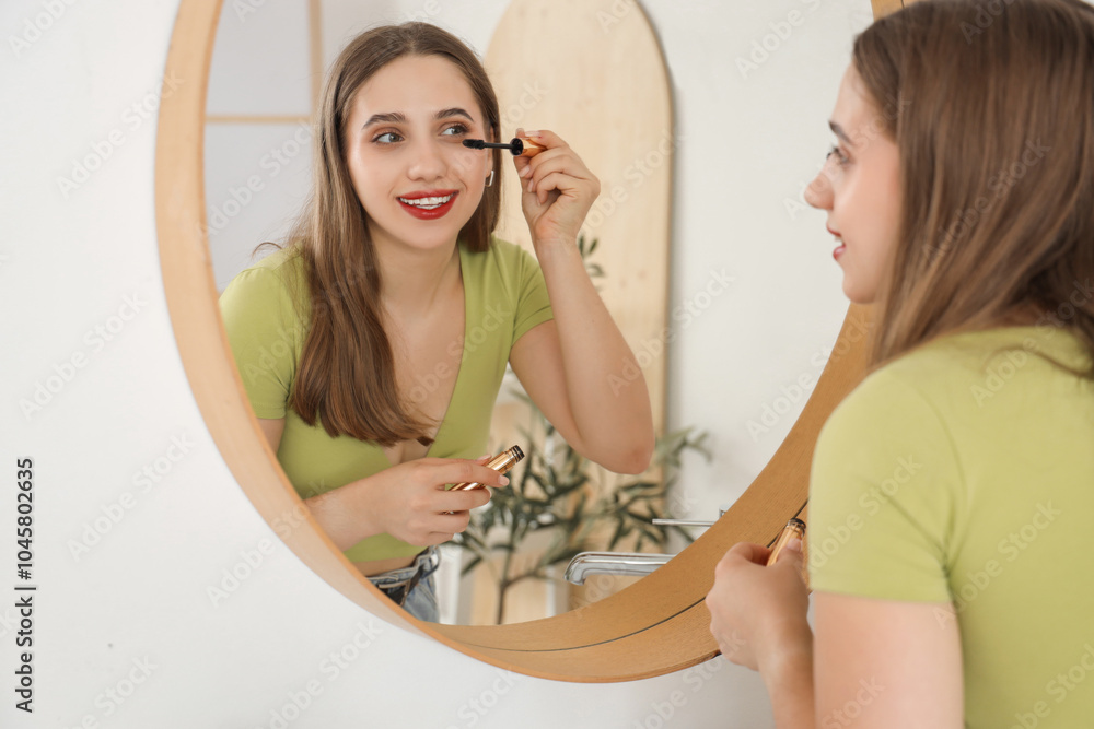 Young woman applying mascara near mirror in bathroom