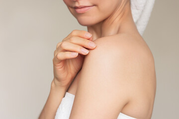 a young caucasian woman wrapped in a white towel after a shower, smiling and gently touching her sho