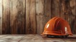 © Dulemegapixel - The image shows an orange hard hat placed on a wooden surface, which creates a rustic and earthy atmosphere, symbolizing construction and labor industries.