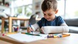 © LifeMedia - A young boy with bandaged arms deeply engrossed in drawing with crayons on paper at a table, enveloped by sunlight pouring through the windows of a bright room.