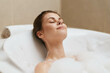 © SHOTPRIME STUDIO - Relaxed woman enjoying a peaceful bath, surrounded by bubbles, eyes closed, experiencing tranquility and self-care in a modern bathroom setting.