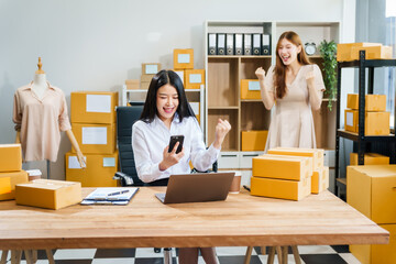 Two young female entrepreneurs work together in warehouse with parcel boxes, wooden tables, and shelves. prepare sales brochures, social media templates, business proposals for small online business.