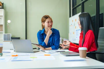 Two young female business consultants work on startup, collaborating on mobile app development social media strategies. whiteboards, documents, they aim to build a successful e-commerce business.