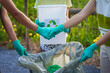 © Phushutter - Close-up of female hands from a family collecting plastic waste and bottles from the ground. They wear gloves and focus on recycling to help reduce plastic pollution and protect the environment.