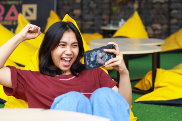 attractive asian woman celebrating winning playing online game tournament using smartphone with raising fist say yes gesture sitting in outdoor cafe