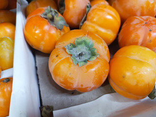 A persimmon with leaves lies in a box in close-up. Harvesting. Selling organic fruits on the market is a concept. The background for the advertisement, the place for the text.