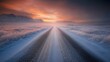 © Sinechana - 2410 115.A straight road blanketed with thin ice and surrounded by wintery fields in southern Iceland, stretching towards distant mountains, with the soft, warm glow of the sunset creating a striking