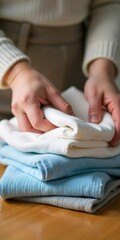 A close-up of a person's hands folding freshly washed and dried clothes on a wooden surface