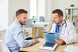 © Studio Romantic - Serious male doctor sitting at desk in office, giving consultation to young man in medical clinic. Professional physician or cardiologist describing treatment plan to male patient during consultation.