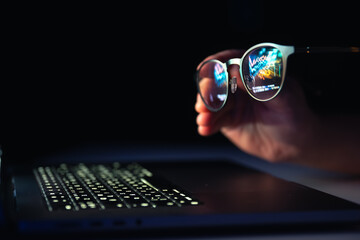 Reflection from a laptop in glasses on a dark background.