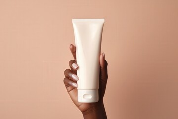 woman hand is holding a white mockup tube of facial cream on a beige isolated background