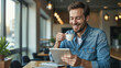 © MrBaks - Cheerful young man holding cup of coffee and using digital tablet in cafe