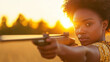 © Bonsales - Young woman takes aim with an air rifle as the sun sets, casting a bright glow behind her