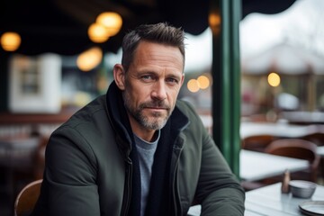 Wall Mural - Portrait of handsome middle-aged man with beard and mustache looking at camera while sitting in outdoor cafe