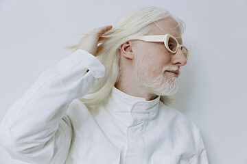 Stylish elderly man with long white hair and glasses poses thoughtfully against a plain white background, showcasing modern fashion and confidence He exudes wisdom and serenity