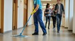 © Anna - Janitor mopping school hallway as students walk by in uniform.