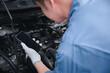 © sorapop - Confident mechanic checking battery at car repair station. Horizontal photo of male technician using smartphone to diagnose engine problems. Indoor shot with garage background.
