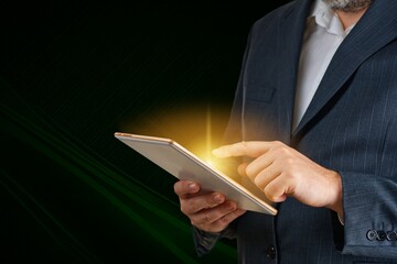 A confident businessman in a sharp suit interacts with a glowing digital tablet, showcasing the blend of technology and innovation in modern business against a dark background.