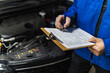 © zphoto83 - A mechanic inspects a vehicle engine while checking a maintenance checklist in a workshop