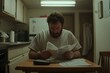 © Alexey - Caucasian man in white t-shirt examining financial documents at kitchen table. Personal debt and bill payment stress concept. Mental health awareness portrait