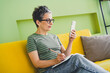 © deagreez - Photo of nice retired female sit sofa write notebook hold device wear green clothes enjoy cozy interior flat indoors