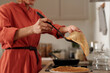 © pressmaster - Person wearing orange robe skillfully flipping pancake in cozy kitchen with wooden countertop and various utensils. Focus on delicious breakfast preparation