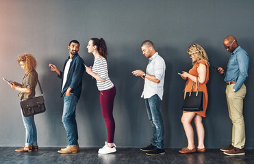Poster - Doing their own thing on their devices. Studio shot of people waiting in line against a grey background.