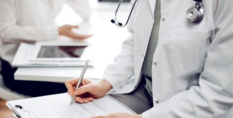 Wall Mural - Doctor and patient view. Female physician is filling up a records from opposite a woman having a medical examination. Medicine concept