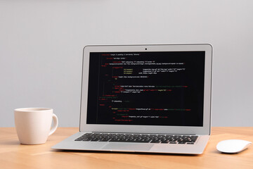 Programmer's workplace. Modern laptop with unfinished code and cup on desk indoors