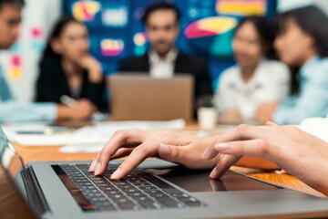 Closeup hand typing keyboard laptop with blurred background of business people using laptop to analyze financial data or data analysis display on screen background. Meticulous