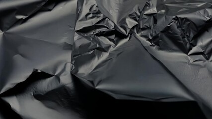 Fototapete - A crumpled black plastic sheet displays various textures and shadows, creating an abstract background. The light enhances its glossy surface, adding depth.