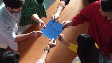 Wall Mural - Top down view of business people gathering jigsaw piece together.Startup team with casual cloth standing at table while gathering puzzle piece. Show unity, cooperation and team working. Convocation.