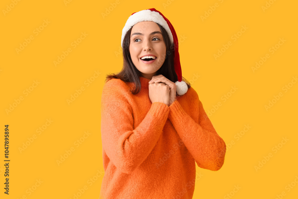 Happy young woman in Santa hat on yellow background