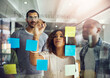 © peopleimages.com - Business, people and writing on glass wall with sticky notes for project strategy, brainstorming or teamwork. Professional, employees and planning creative ideas, kpi solution or discussion in office