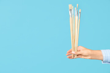 Wall Mural - Hand of female artist with brushes on blue background