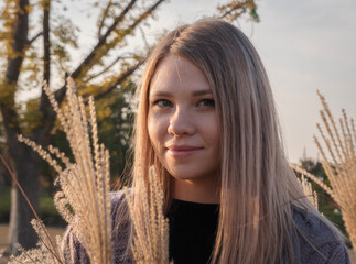 A young woman poses amidst tall grass on a sunny autumn day in the park