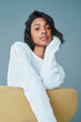 © peopleimages.com - Relax, trendy and fashion with portrait of woman in studio for casual, gen z and calm. Youth, student and peace with Indian person sitting on chair on blue background for confidence, cool and clothes
