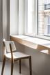 © JuanM - A cozy reading nook with a wooden chair by a sunlit window in a modern interior