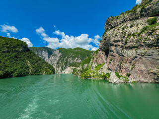 Scenic ferry boat tour on Lake Koman reservoir on Drin river surrounded by forested steep hills, cliffs and majestic rugged mountain ranges of Albanian Alps. Panoramic view along Albanian Fjords. Awe