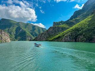 scenic ferry boat tour on lake koman reservoir on drin river surrounded by forested steep hills, cli