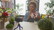 © Krakenimages.com - African american woman florist holding orchid and gift box in a flower shop interior, recording a video.