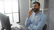 © Krakenimages.com - Handsome man talking on phone in a modern office with shelves in background and computer on desk